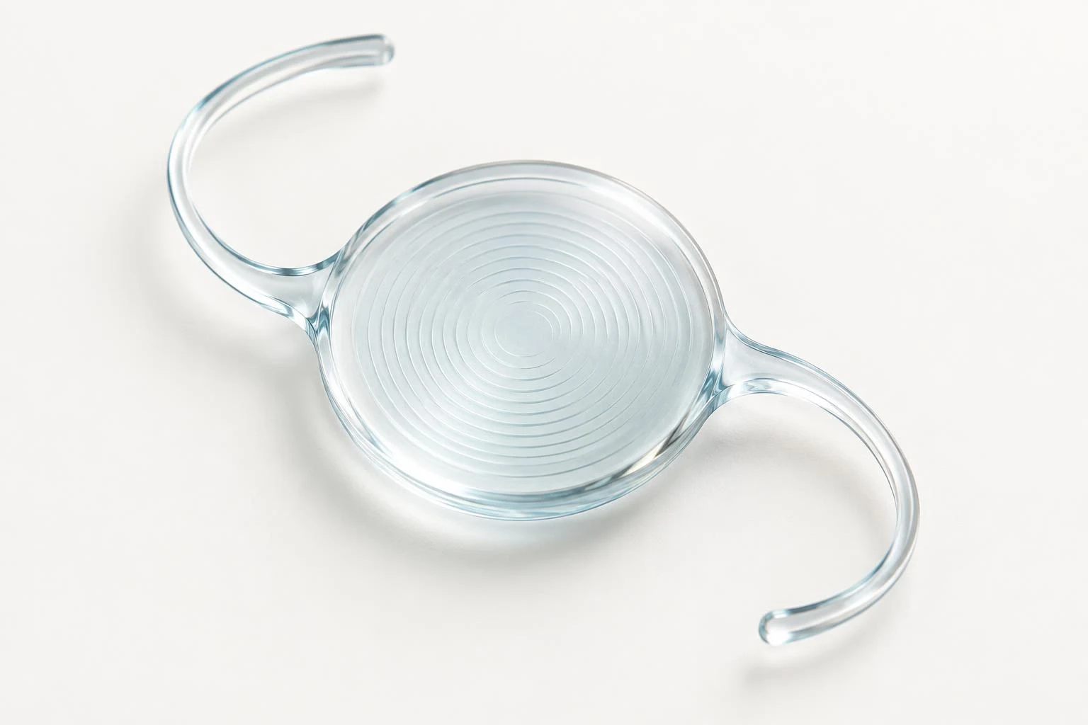 Imagen generada de un lente intraocular multifocal transparente, con anillos concéntricos y dos hápticas curvas.
